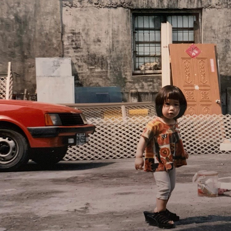 Photo of illustrator Gracey Zhang as a child: A small child in a colourful shirt and wearing adult sandals stands in the foreground.